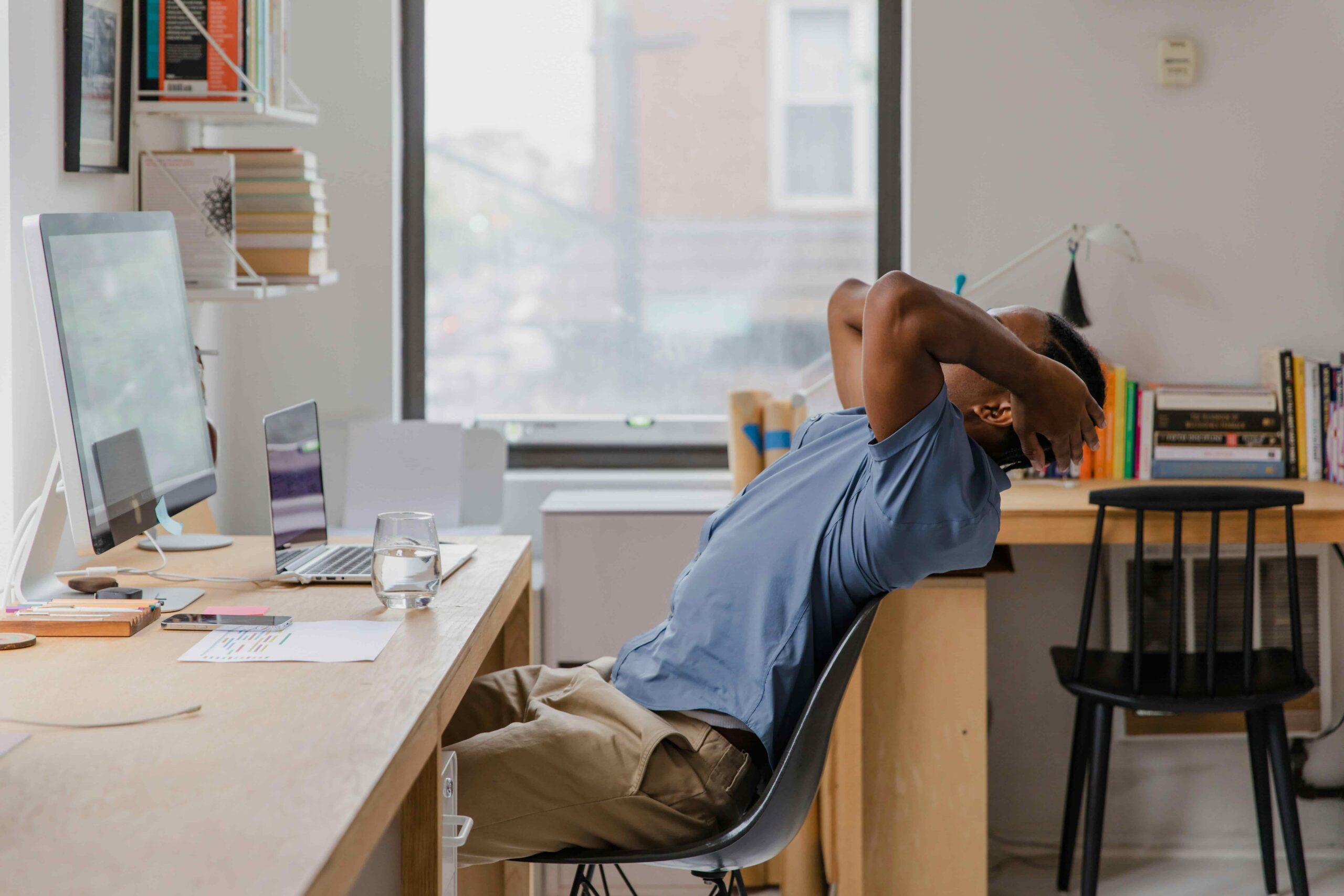 A man at a desk stretches over the back with his hands behind his head